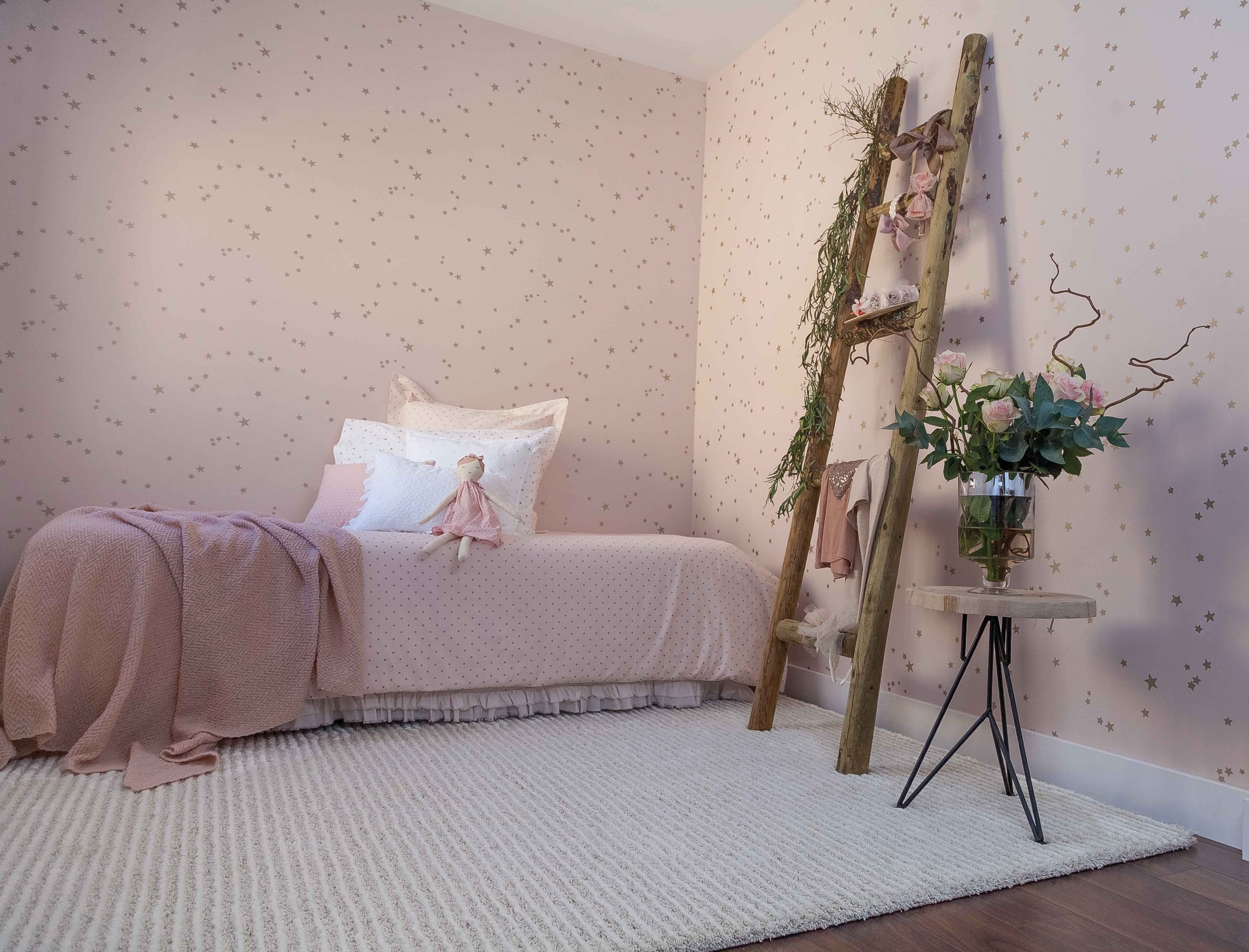 Ambiente decorado siguiendo las directrices del neurointeriorismo, con un dormitorio que tiene una acogedora alfombra, una escalera decorativa y una mesita con un jarrón y planta, junto a la cama
